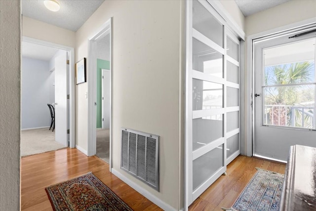 hall featuring baseboards, wood finished floors, visible vents, and a textured ceiling