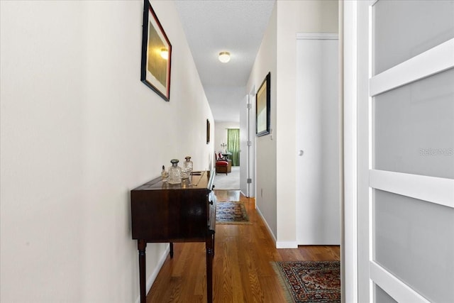hallway featuring a textured ceiling, baseboards, and wood finished floors