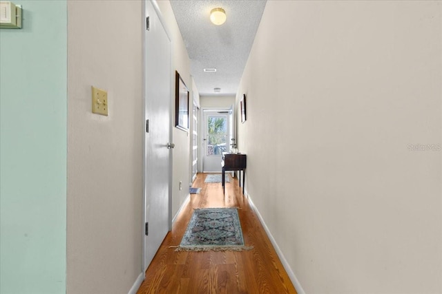 corridor featuring baseboards, a textured ceiling, and wood finished floors