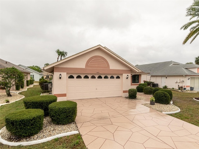 single story home featuring concrete driveway, a garage, central AC, and stucco siding