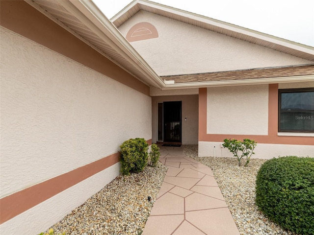 doorway to property featuring stucco siding and roof with shingles