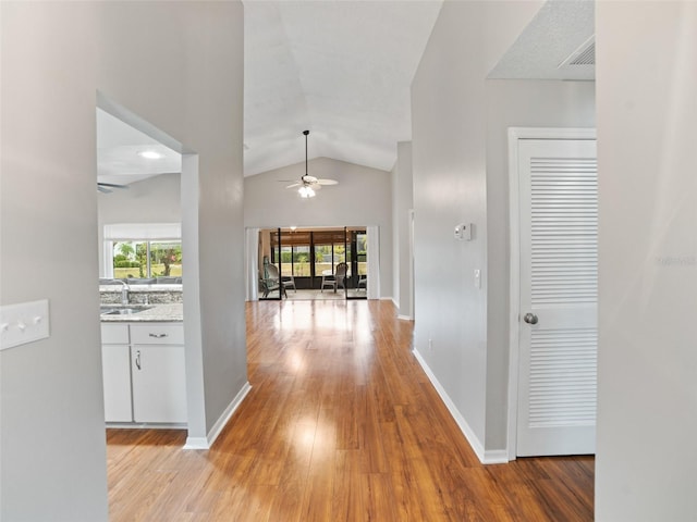 hallway featuring light wood-type flooring, visible vents, high vaulted ceiling, a sink, and baseboards