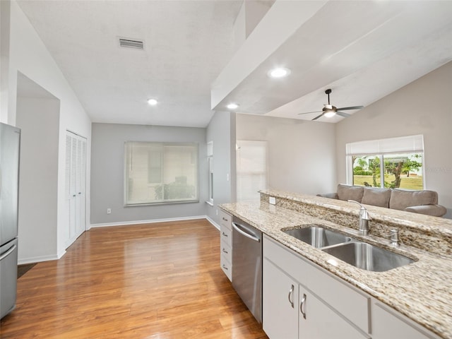 kitchen featuring light wood-style flooring, a sink, light stone counters, open floor plan, and appliances with stainless steel finishes