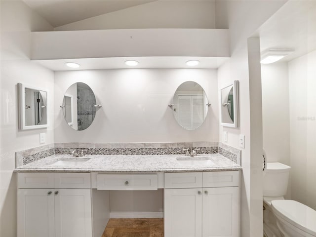 full bath featuring double vanity, toilet, vaulted ceiling, and a sink