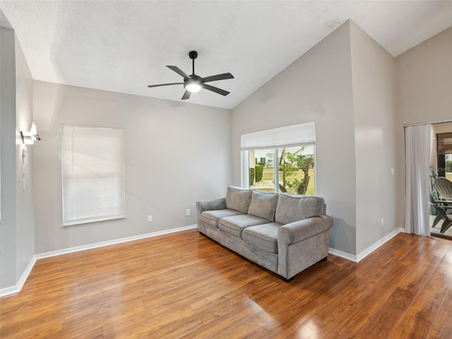 living area featuring baseboards, high vaulted ceiling, wood finished floors, and a ceiling fan