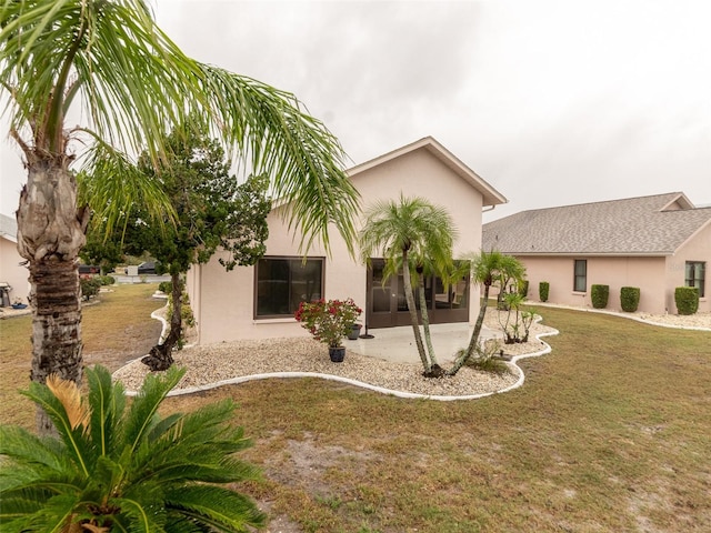 rear view of house with stucco siding, a yard, and a patio area