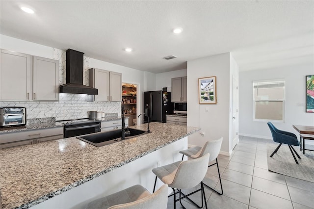 kitchen featuring electric range, gray cabinets, black fridge, a sink, and wall chimney range hood