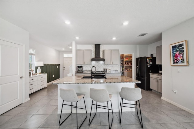 kitchen featuring a breakfast bar, gray cabinets, a sink, freestanding refrigerator, and wall chimney exhaust hood