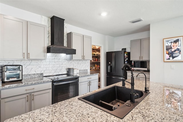 kitchen featuring visible vents, gray cabinetry, black appliances, and wall chimney exhaust hood