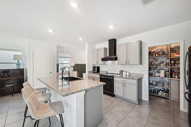 kitchen featuring black / electric stove, a sink, a kitchen breakfast bar, wall chimney exhaust hood, and tasteful backsplash