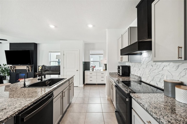 kitchen featuring light stone countertops, a sink, decorative backsplash, black appliances, and wall chimney exhaust hood