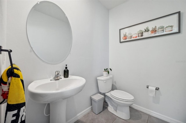 half bath featuring tile patterned floors, toilet, baseboards, and a sink