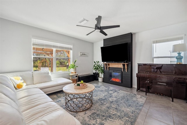 tiled living area with visible vents, a ceiling fan, and a glass covered fireplace