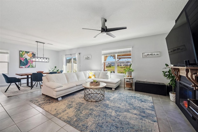 tiled living area featuring a textured ceiling, a glass covered fireplace, and a ceiling fan