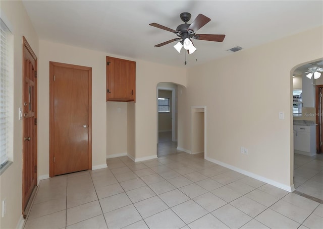 spare room featuring visible vents, baseboards, light tile patterned floors, arched walkways, and a ceiling fan