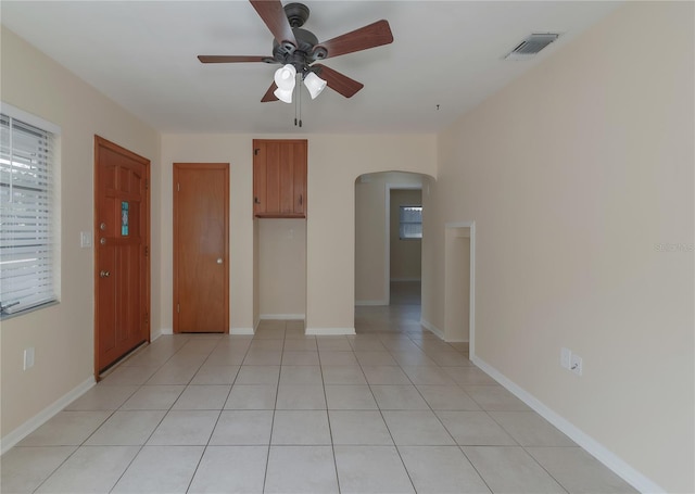 interior space with light tile patterned floors, baseboards, visible vents, arched walkways, and ceiling fan