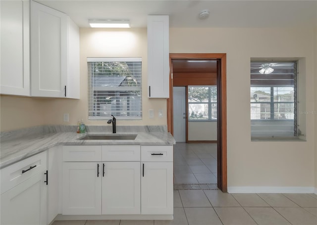 kitchen with baseboards, light stone countertops, light tile patterned floors, white cabinetry, and a sink