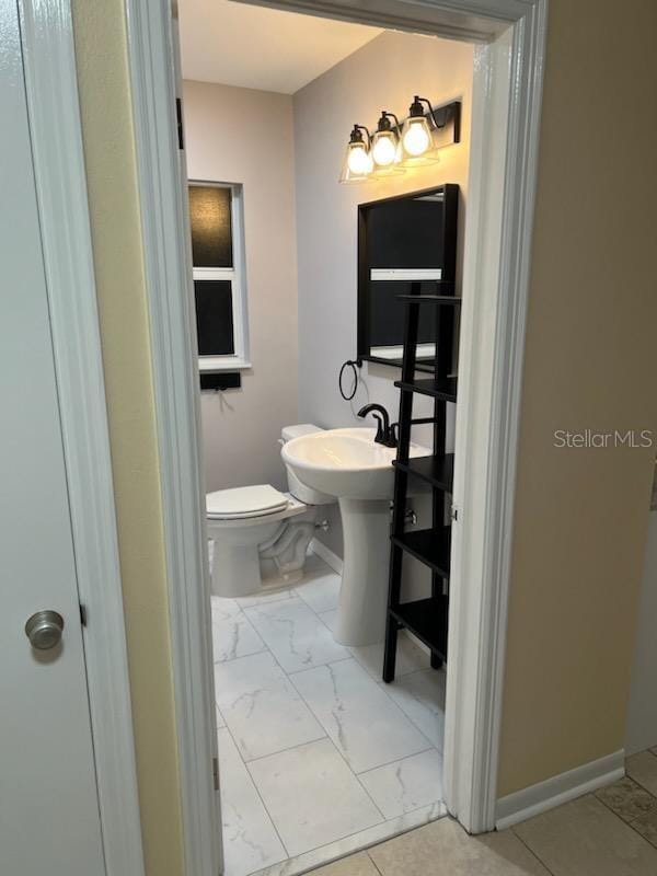 bathroom with baseboards, toilet, and marble finish floor