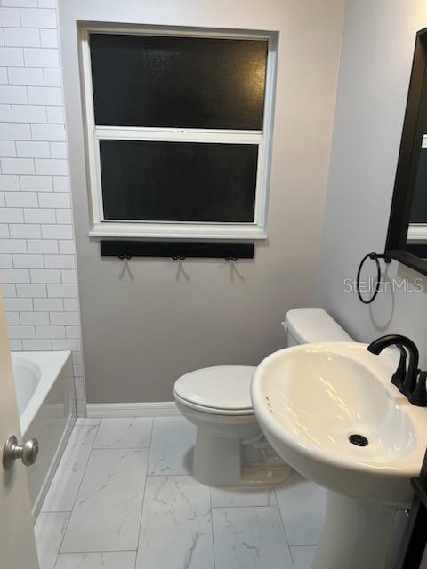 bathroom featuring toilet, baseboards, marble finish floor, and a sink