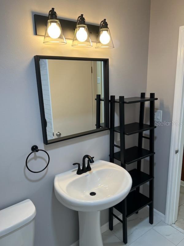 half bathroom featuring toilet, baseboards, marble finish floor, and a sink