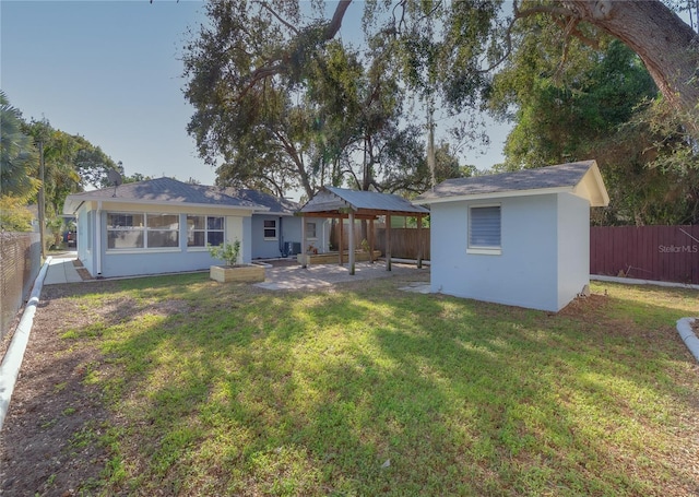 rear view of property with a gazebo, stucco siding, an outdoor structure, a yard, and a fenced backyard