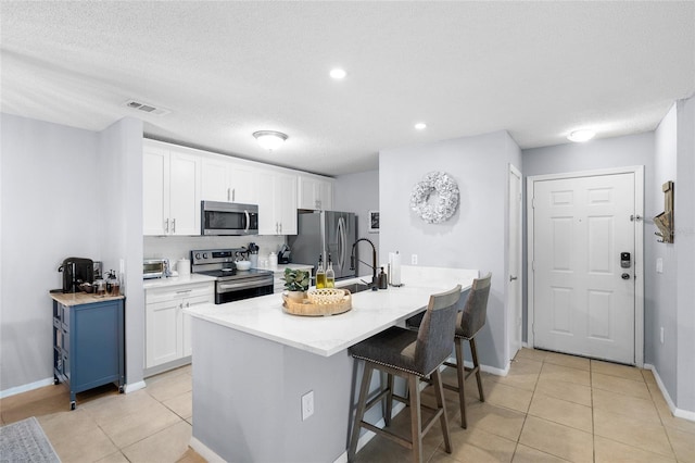 kitchen featuring light tile patterned floors, white cabinetry, appliances with stainless steel finishes, and a breakfast bar