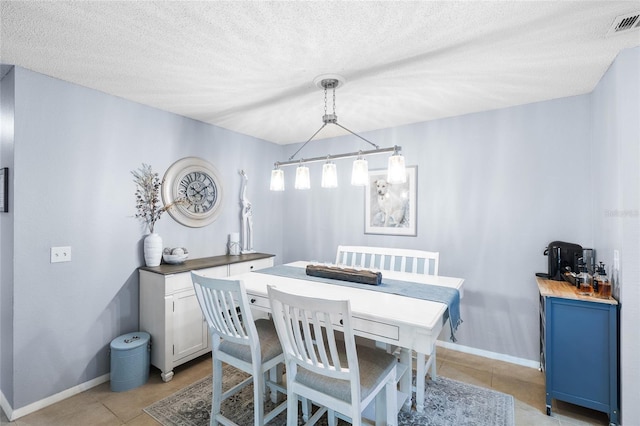 dining space with light tile patterned floors, baseboards, visible vents, and a textured ceiling