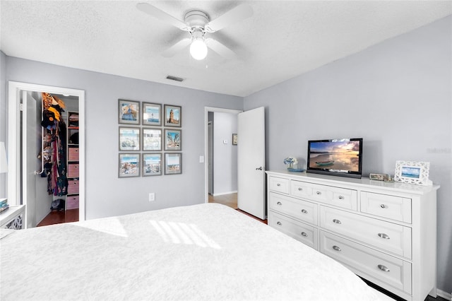 bedroom featuring visible vents, a walk in closet, ceiling fan, a closet, and a textured ceiling