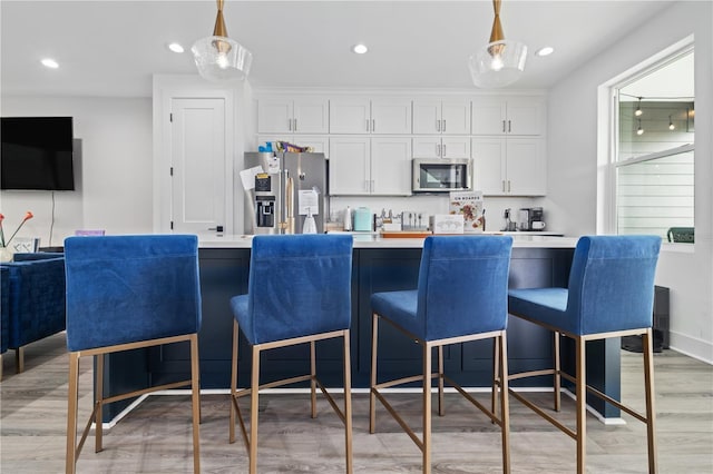 kitchen with light wood-style flooring, decorative light fixtures, open floor plan, white cabinetry, and appliances with stainless steel finishes