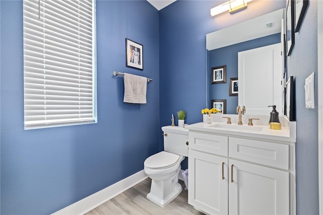 half bath featuring visible vents, toilet, wood finished floors, baseboards, and vanity