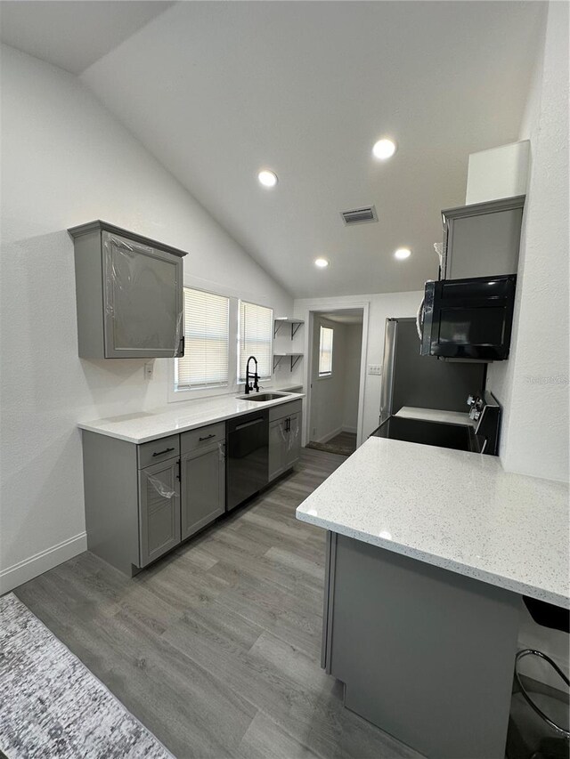 kitchen with vaulted ceiling, gray cabinetry, black appliances, and a sink