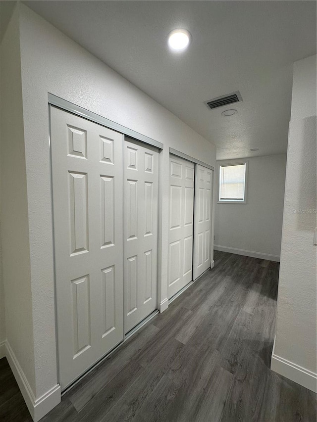 unfurnished bedroom featuring visible vents, multiple closets, baseboards, and dark wood-style flooring