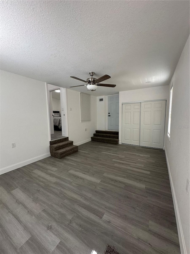 unfurnished living room with ceiling fan, baseboards, dark wood-style flooring, and a textured ceiling