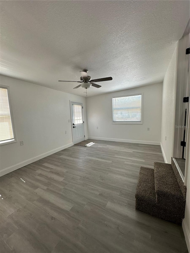 unfurnished living room with ceiling fan, baseboards, a textured ceiling, and wood finished floors