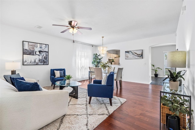 living room with visible vents, baseboards, dark wood-style floors, ceiling fan with notable chandelier, and arched walkways