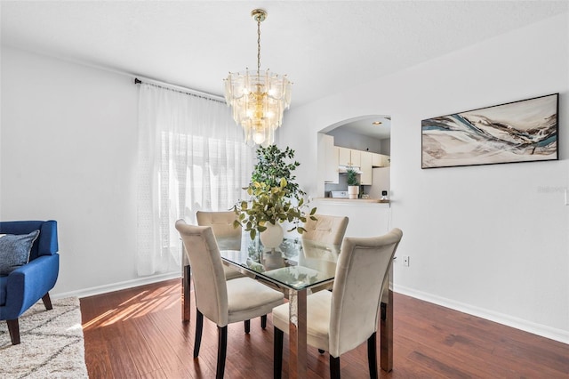 dining space featuring baseboards, arched walkways, a notable chandelier, and wood finished floors