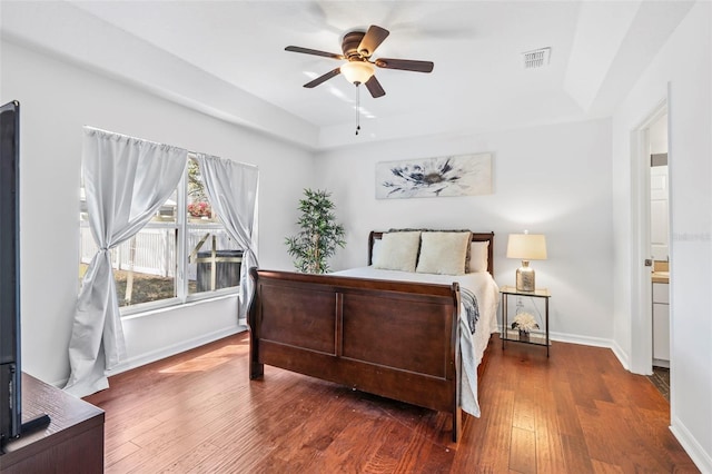 bedroom with a ceiling fan, baseboards, visible vents, a tray ceiling, and hardwood / wood-style flooring