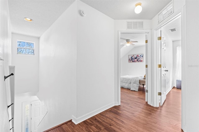 hall with visible vents, a textured ceiling, and wood finished floors