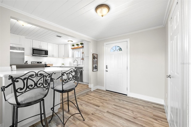 kitchen with a kitchen breakfast bar, white cabinetry, appliances with stainless steel finishes, crown molding, and light wood finished floors