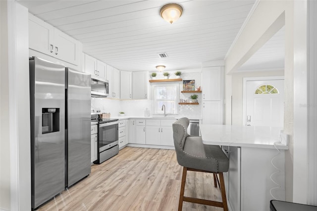 kitchen with a kitchen breakfast bar, appliances with stainless steel finishes, white cabinets, and light countertops