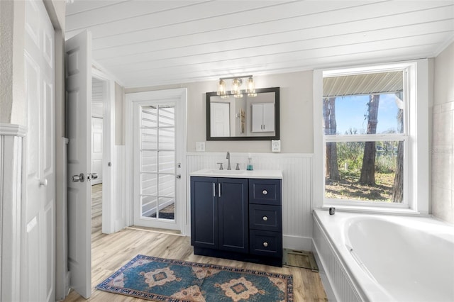 bathroom featuring a notable chandelier, a garden tub, wood finished floors, wainscoting, and vanity