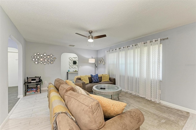 living area featuring visible vents, arched walkways, ceiling fan, a textured ceiling, and light wood-type flooring