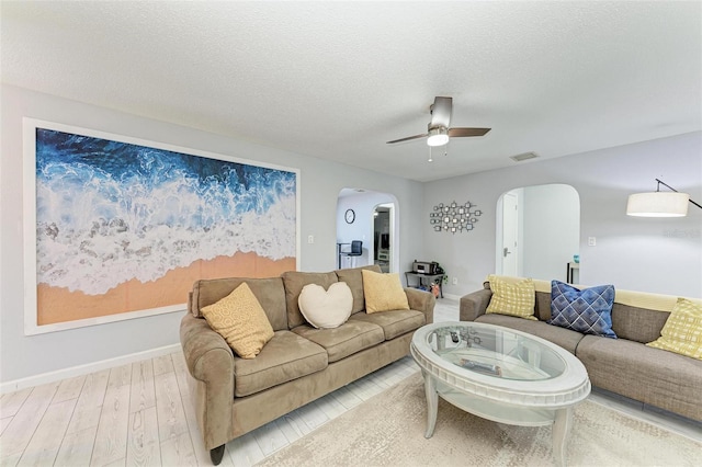 living area featuring light wood finished floors, visible vents, arched walkways, a textured ceiling, and a ceiling fan