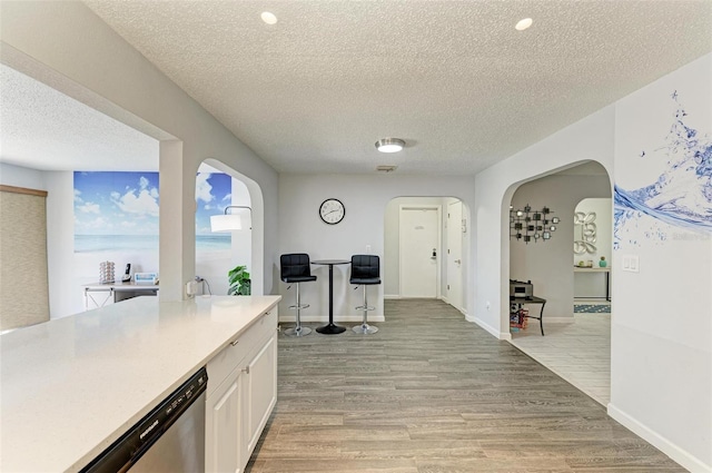 kitchen with arched walkways, light wood-style floors, stainless steel dishwasher, and white cabinets