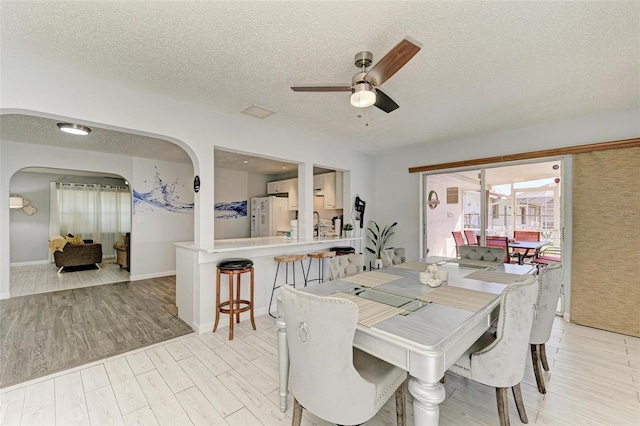 dining space featuring ceiling fan, light wood-style flooring, arched walkways, and a textured ceiling