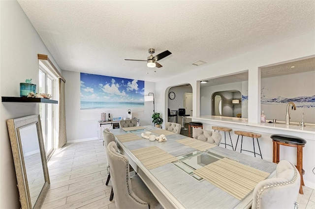 dining area with light wood-type flooring, a textured ceiling, arched walkways, baseboards, and ceiling fan