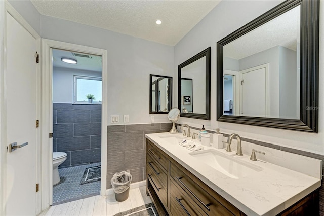 full bath with a sink, a textured ceiling, tile walls, and toilet