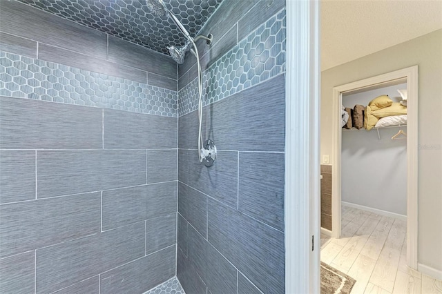 full bath featuring a walk in closet, tiled shower, baseboards, and wood finished floors