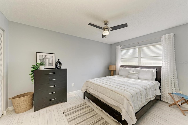 bedroom with light wood-type flooring, baseboards, a textured ceiling, and ceiling fan