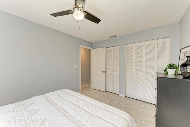 bedroom featuring wood finish floors, visible vents, multiple closets, a textured ceiling, and ceiling fan